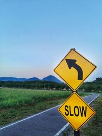 Road sign on field against clear blue sky