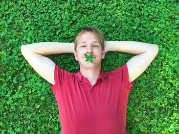 Portrait of man lying on plants with leaves in mouth