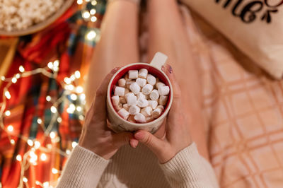 Cup of cocoa or coffee drink with marshmallows in female holding hands over the legs of woman