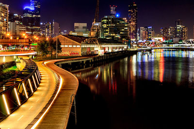 Illuminated bridge over river by buildings at night