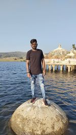 Full length of young man standing on rock against sky