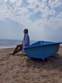 Woman sitting on boat at beach against sky