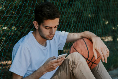 Boy looking at the phone with basketball ball outdoors