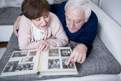 Senior couple lying on couch, looking at photo album