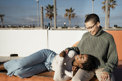 Young woman lying on friends lap while sitting on bench