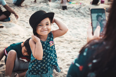 Mother photographing daughter with mobile phone by boy at beach