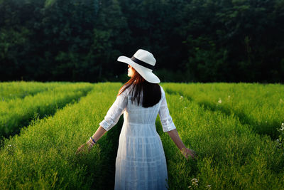 Back view of woman in white dress holding white hat walking at the green cutter flowers field.