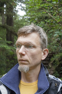 Thoughtful mature man standing against trees