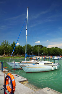 Sailboats moored at harbor against blue sky