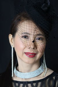 Close-up portrait of woman wearing lipstick and jewelry against black background