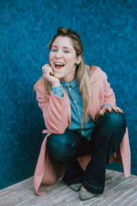 Portrait of cheerful young woman crouching against wall