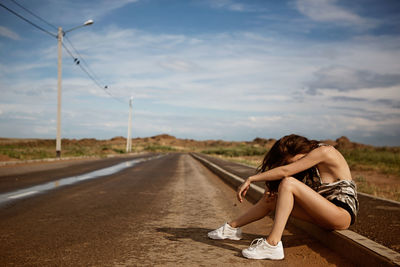 Woman sitting on road against sky