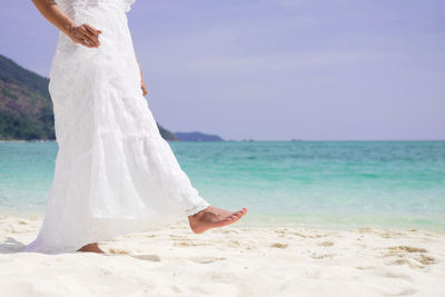 Low section of woman standing on beach against sea