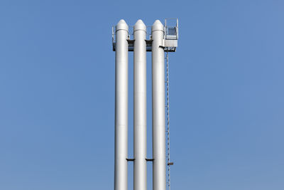 Low angle view of storage tanks against clear blue sky