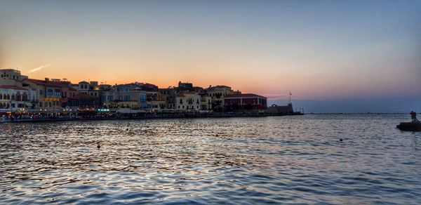 Buildings by sea against clear sky during sunset