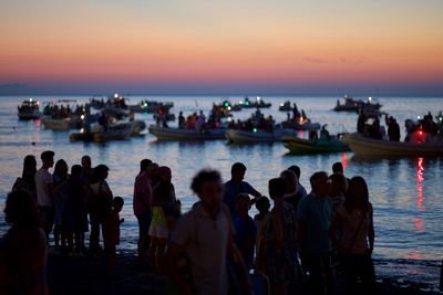 People at beach against sky during sunset