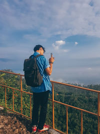 Man photographing on railing against sky