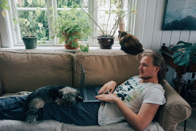 Man using laptop with dog relaxing on lap at home