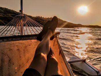 Low section of man on boat at sea during sunset