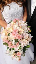 Midsection of bride holding bouquet with groom