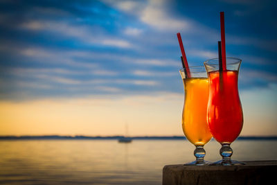 Drinks on wood against sea during sunset