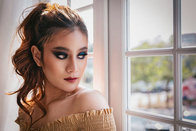 Close-up portrait of young woman looking through window