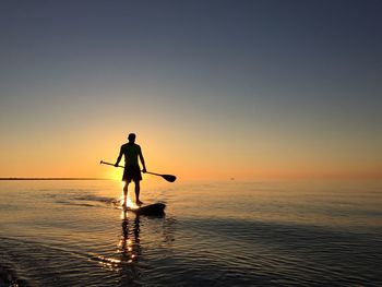 Silhouette of man fishing in sea against sunset sky