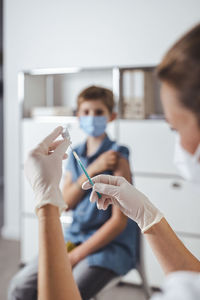 Nurse preparing vaccine injection for boy in background
