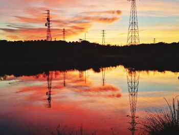 Silhouette electricity pylon by lake against sky during sunset