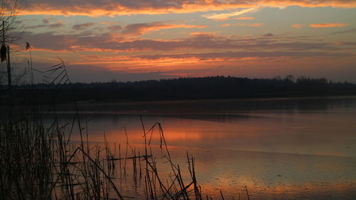 Scenic view of lake against dramatic sky during sunset