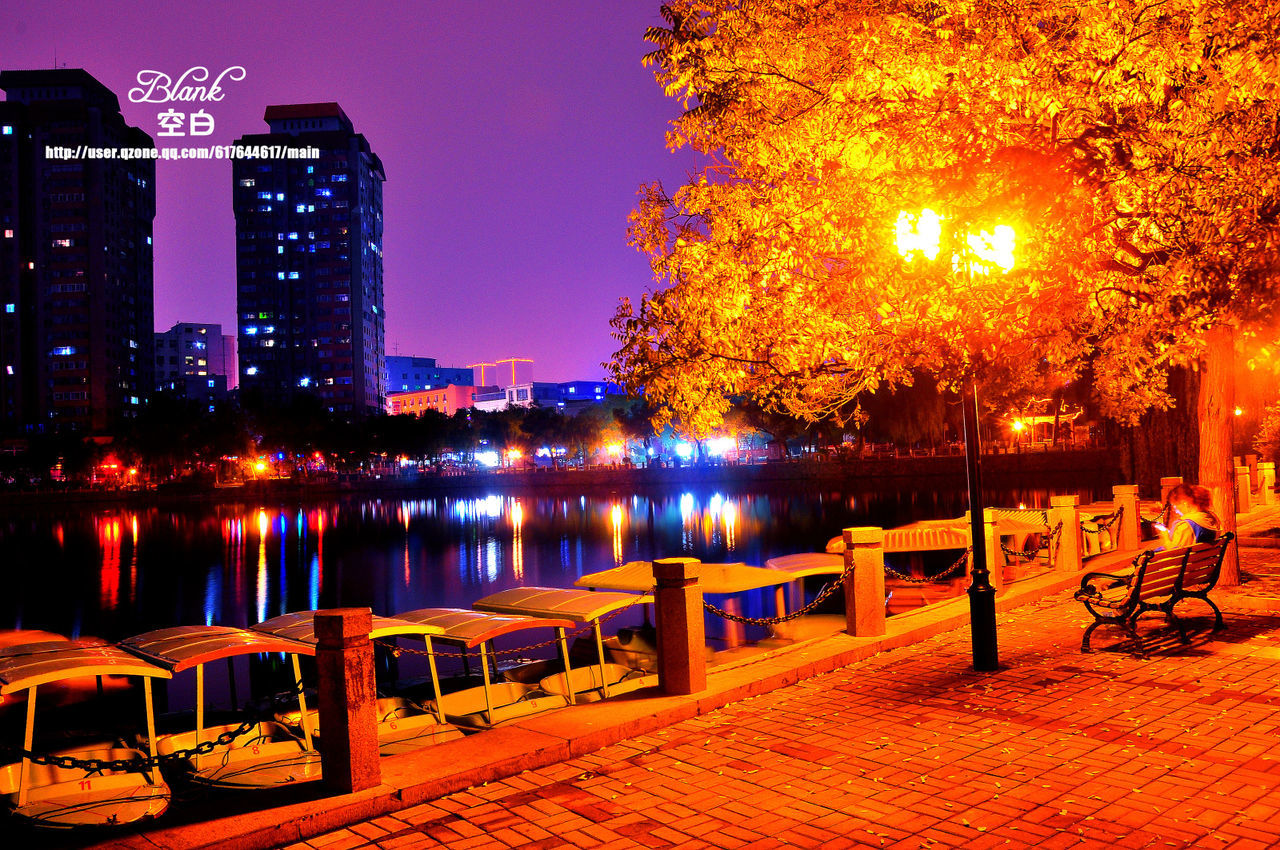 railing, illuminated, water, city, built structure, tree, building exterior, architecture, river, clear sky, sunset, street light, night, bench, orange color, lake, reflection, outdoors, bridge - man made structure, sky