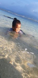 Portrait of boy in water at beach against sky