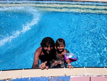 High angle portrait of smiling father and son swimming in pool