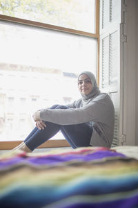 Muslim woman wearing a hijab sitting in a window sill