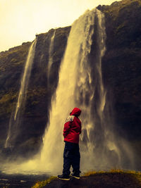Side view of man standing against waterfall