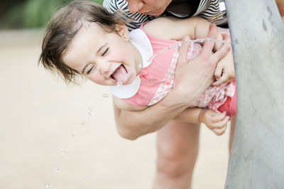 Woman holding daughter drinking water from fountain