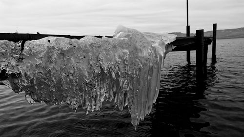 Wooden posts on frozen sea against sky