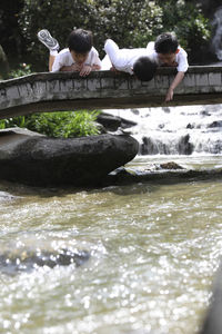 Boys lying on footbridge over stream
