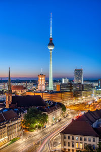 Illuminated buildings in city against clear blue sky