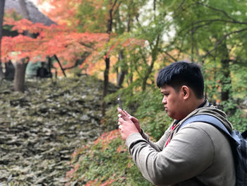Side view of young man standing against trees in forest