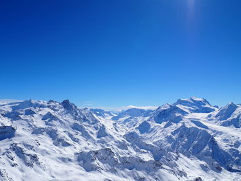Scenic view of snow covered mountains against clear blue sky