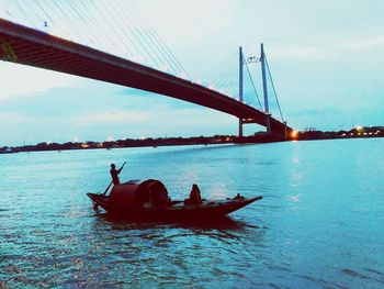 People on suspension bridge over sea against sky