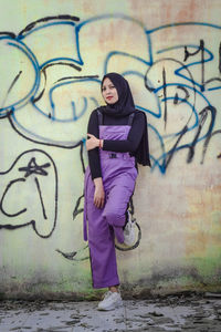 Full length of woman standing against graffiti wall