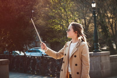 Girl holding monopod while taking selfie through smart phone during winter