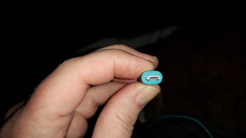 Close-up of hand holding clock against black background