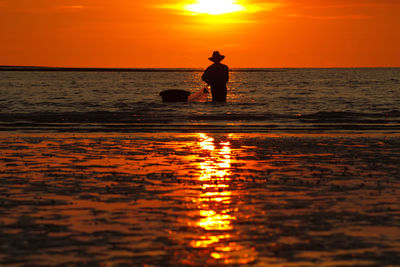 Silhouette man standing on beach against orange sky