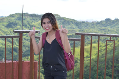 Portrait of smiling young woman standing against railing