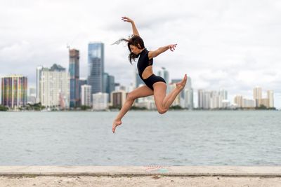 Full length of woman jumping in city against sky