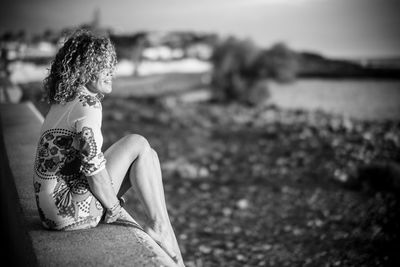 Side view of smiling mature woman sitting on retaining wall at beach