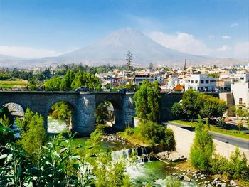 Bridge over river by buildings in city against sky